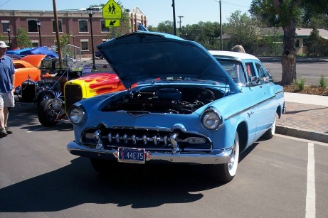 1972 Ford Ranchero - A blue sedan is parked with its hood open, alongside other vehicles at an outdoor event.