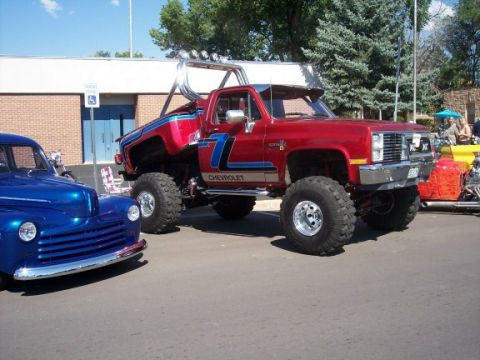 1972 Ford Ranchero - A heavily modified red Chevrolet pickup truck with custom graphics and a roll bar is parked next to a blue vintage car.