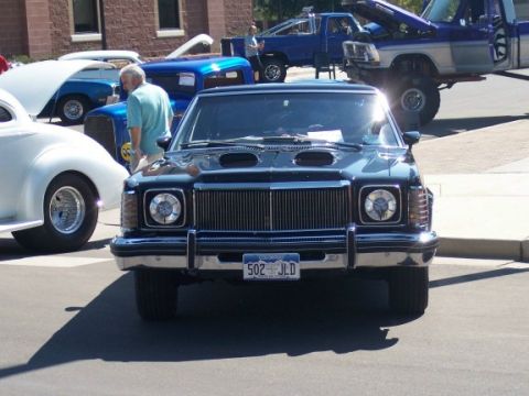 1972 Ford Ranchero - A dark sedan with prominent hood scoops is parked at an outdoor event, with other vehicles visible in the background.