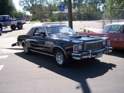 1972 Ford Ranchero - A black 1977 Ford Ranchero is parked next to another vehicle, with a blue pickup truck in the background.