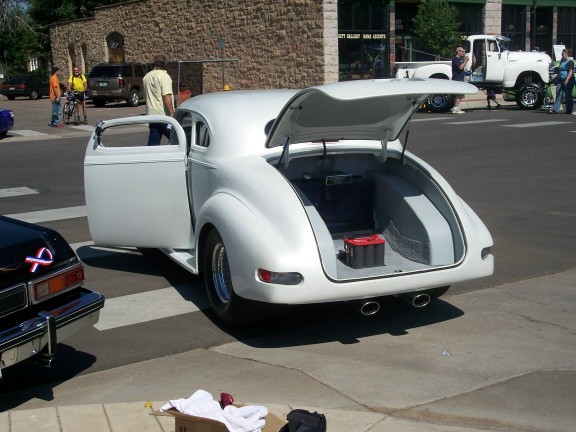 White coupe with open doors and trunk, showing a red battery in the cargo area