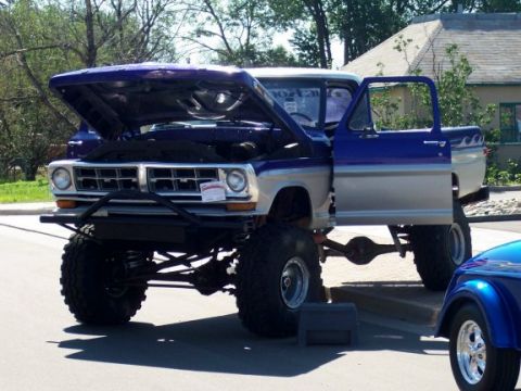 1972 Ford Ranchero - A custom lifted pickup truck is displayed with its hood and driver's door open, parked beside another vehicle.
