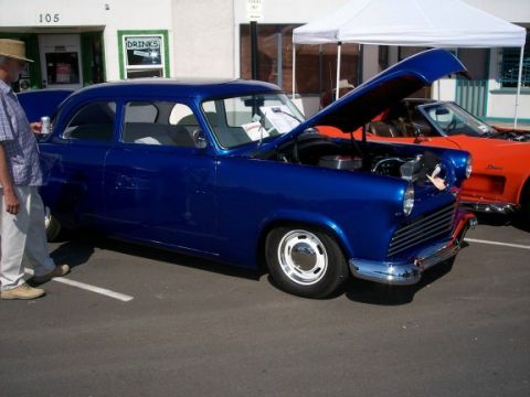 1972 Ford Ranchero - A blue sedan is parked with its hood open, alongside another vehicle under a white canopy.