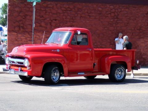 1972 Ford Ranchero - This red 1956 Ford F-100 pickup truck is parked on a street with a brick building in the background.