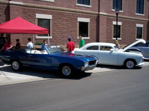 1972 Ford Ranchero - Two classic cars are parked outside a brick building, one a blue convertible and the other a white sedan.