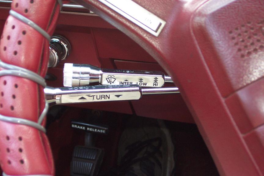 Chrome turn signal and wiper stalk levers on red steering column of classic car