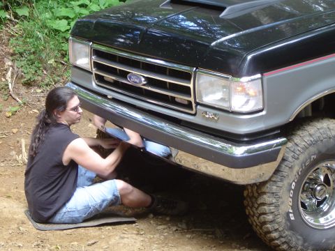 1989 Ford Bronco - A person works on the front bumper of a 1989 Ford Bronco, which has a chrome bumper and a 4x4 badge.