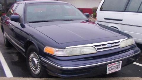 1995 Ford Crown Victoria - A dark blue 1995 Ford Crown Victoria is parked, showing its front 3/4 view with a visible license plate.