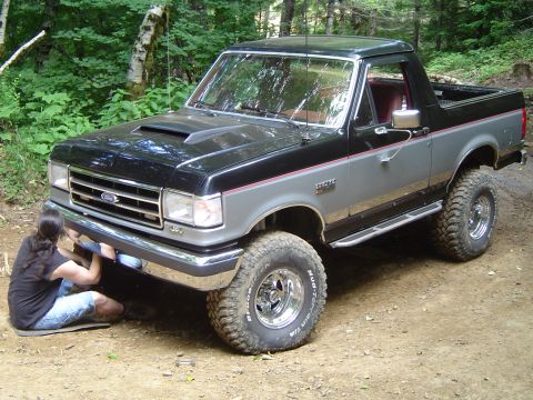1989 Ford Bronco - Person works on the front bumper of a two-tone 1989 Ford Bronco off-road.