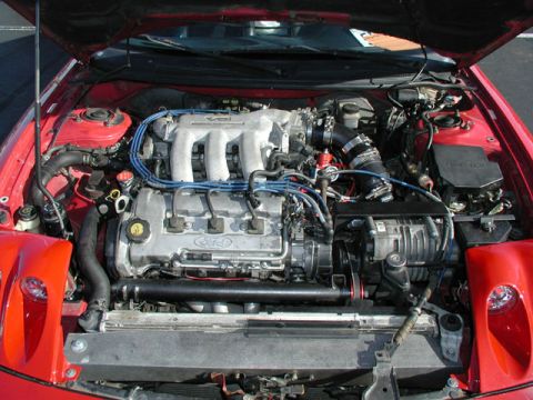1991 Ford Probe - Open engine bay of a red car showing a transverse Ford V6 with a cast-aluminum intake manifold, Ford-oval cam cover, blue spark plug wires…