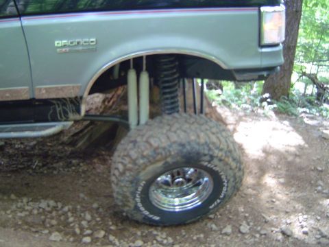 1989 Ford Bronco - A lifted 1989 Ford Bronco is shown with its front wheel and suspension system visible on a dirt trail.