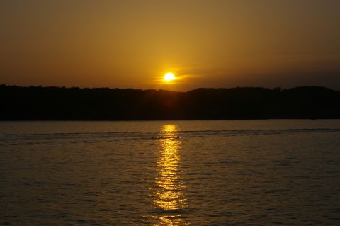 1998 Jeep TJ - A tranquil sunset scene unfolds over calm waters, with a dark tree line silhouetted against the vibrant sky.