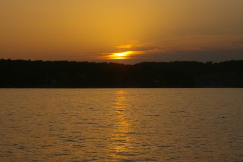 1998 Jeep TJ - A sunset casts a golden glow over the water, with a dark tree line forming the horizon.