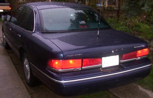 Dark blue Ford Crown Victoria from rear with brake lights on in driveway at dusk