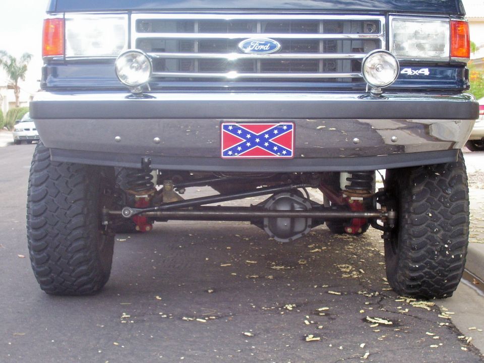 Front of lifted dark blue Ford 4x4 showing solid front axle, chrome bumper and mud tires