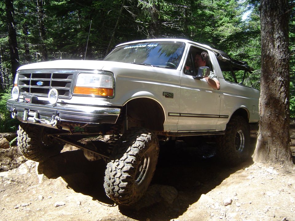 White topless lifted Ford Bronco 4x4 flexing over rocks on a wooded trail with driver