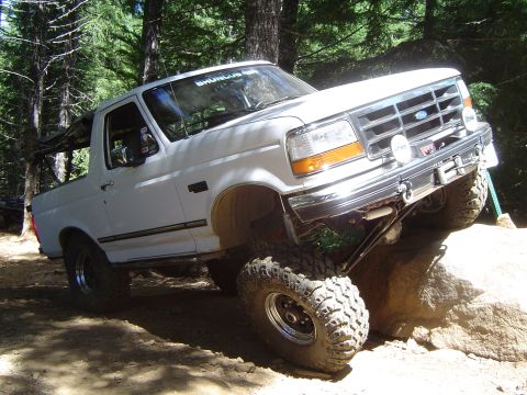 1989 Ford Bronco - This white Ford Bronco is navigating a rocky obstacle on a wooded trail.
