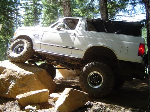 1989 Ford Bronco - This modified SUV is navigating a challenging rocky terrain on a wooded trail.