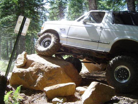 1989 Ford Bronco - A white 1989 Ford Bronco navigates a rocky trail with its tires elevated.