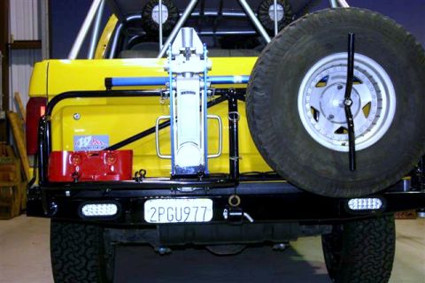 1984 Ford Bronco - Rear view of a yellow SUV equipped with a spare tire, jack, and auxiliary fuel can.