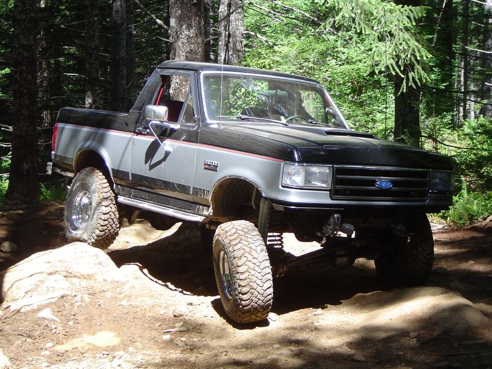 Two-tone grey and black 1989 Ford Bronco on a rocky, wooded trail
