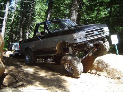 1989 Ford Bronco - A modified Ford Bronco navigates a rocky trail in a wooded area.