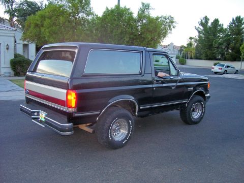 1991 Ford Bronco - Three-quarter rear view of a dark maroon full-size Ford Bronco with a body-color hardtop, silver and red bodyside stripe, and chrome bumper…