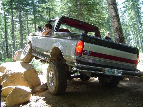 1989 Ford Bronco - A modified Ford Bronco navigates a rocky obstacle on a wooded trail.
