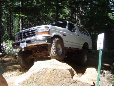 1989 Ford Bronco - A white Ford Bronco navigates a rocky off-road course in a forest setting.