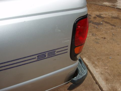 1994 Mazda B3000 - The rear side of a silver pickup truck shows a blue 'SE' decal and scuffs near the taillight.
