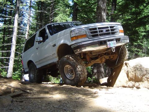 1989 Ford Bronco - White Ford Bronco tackles a challenging rock obstacle during an off-road excursion.