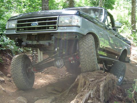 1989 Ford Bronco - Modified 1989 Ford Bronco navigating an off-road obstacle on a wooded trail.