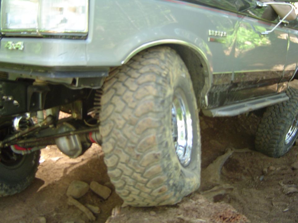 Lifted gray Ford 4x4 front wheel flexing on dirt trail with muddy mud-terrain tire and chrome wheel