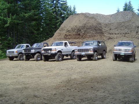1989 Ford Bronco - Several modified Ford trucks and SUVs are parked in a line in front of a large dirt pile.