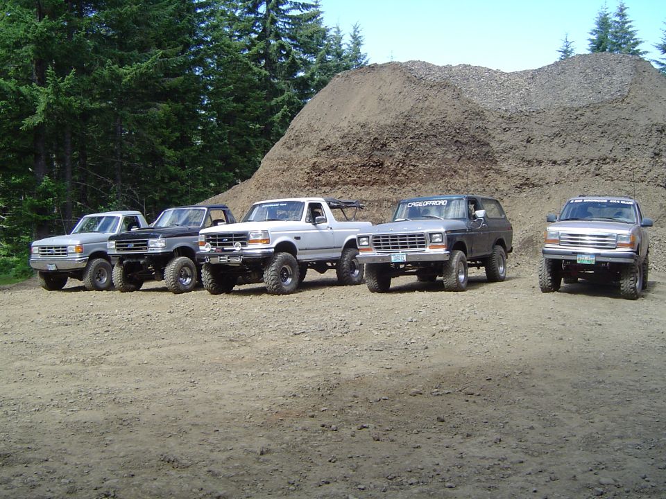 Five lifted Ford Broncos and pickups lined up in a gravel pit beside a dirt pile