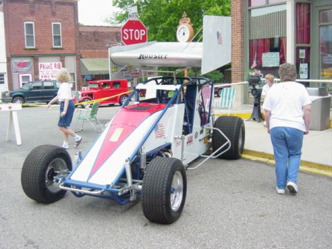 1995 Ford Probe - An open-wheel race car with a large rear wing is displayed on a street, with another car visible in the background.