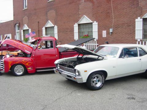 1995 Ford Probe - A white coupe and a red truck with flames are displayed at a car show.
