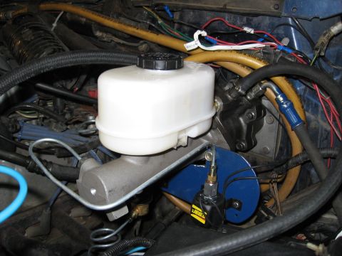 1994 Ford Bronco - Close-up of a vehicle's brake master cylinder assembly, showing fluid reservoir and hydraulic lines.