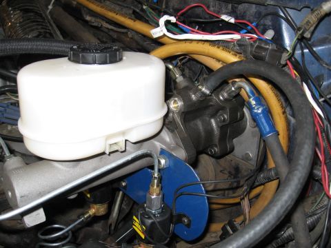 1994 Ford Bronco - Close-up view of the brake master cylinder and booster assembly, showing various hoses and a blue mounting bracket.