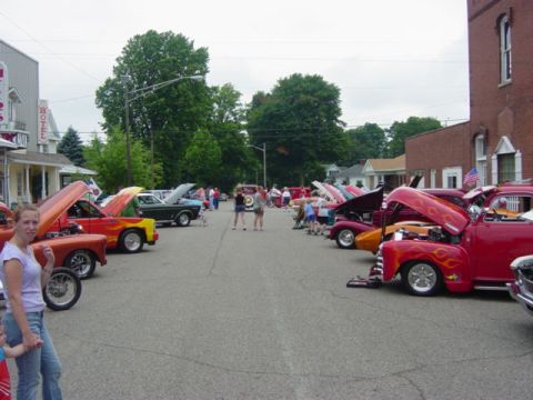 1995 Ford Probe - A street is filled with cars with their hoods open at a car show, with spectators milling about.