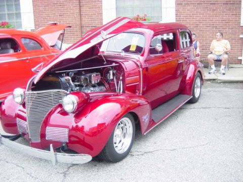 1995 Ford Probe - A shiny red sedan from 1939 is displayed with its hood open, revealing the engine, at a car show.