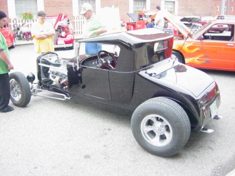 1995 Ford Probe - A black hot rod is displayed at a car show with other vehicles in the background.