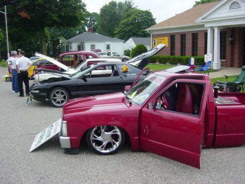 1995 Ford Probe - Several vehicles are on display at an outdoor car show, including a red pickup truck and a black sports car.