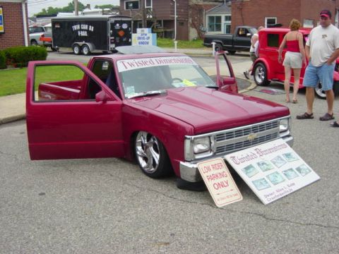 1995 Ford Probe - A red pickup truck with custom modifications is parked at an outdoor event, with people and other vehicles in the background.