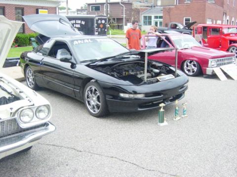 1995 Ford Probe - A black Ford Probe is displayed with its hood open, alongside trophies, at an outdoor car show.