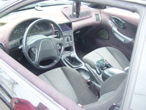 1995 Ford Probe - Interior view of a 1995 Ford Probe, the dashboard, steering wheel, and a game controller on the passenger seat.