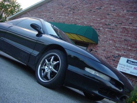 1995 Ford Probe - A black sports coupe is parked in front of a brick building with a green awning. A sign is visible on the right.