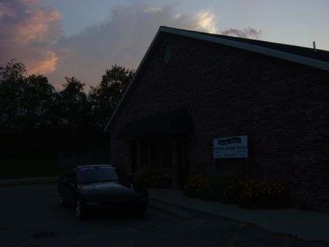 1995 Ford Probe - A dark car is parked in front of a brick building as the sky darkens.