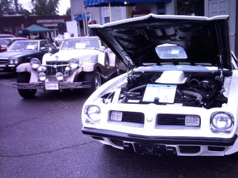 1995 Ford Probe - A white classic car is displayed with its hood open, revealing the engine compartment, while another vintage vehicle is parked nearby.