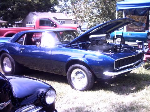 1995 Ford Probe - A blue 1967 Chevrolet Camaro is displayed with its hood open, revealing a powerful engine, while another car sits in front.
